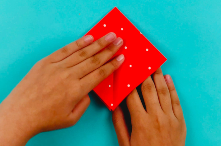 Two hands refolding the paper into a kite shape.