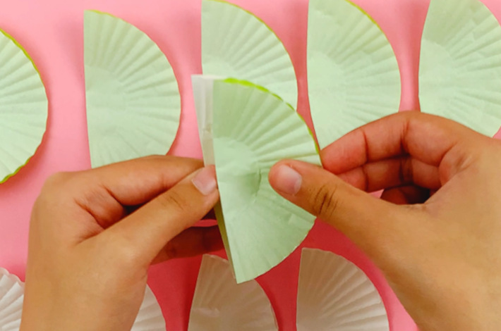 Two hands sticking a green cup cake liner on top of the first white one.