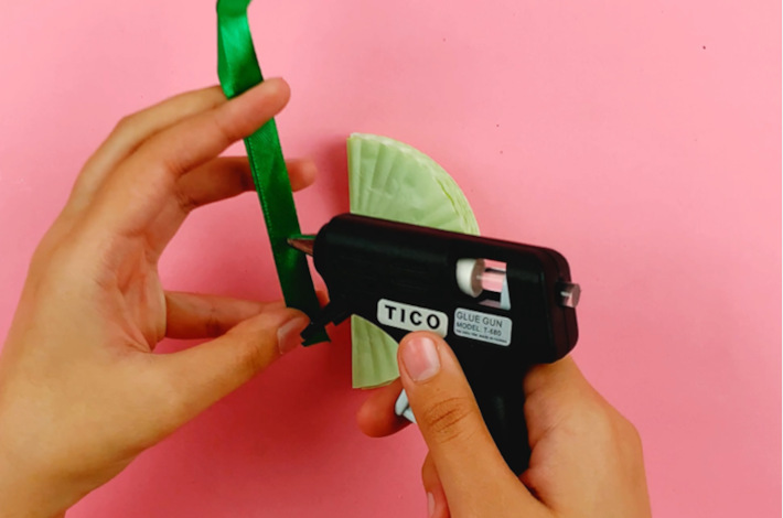 Two hands folding a green ribbon in half and applying some glue.
