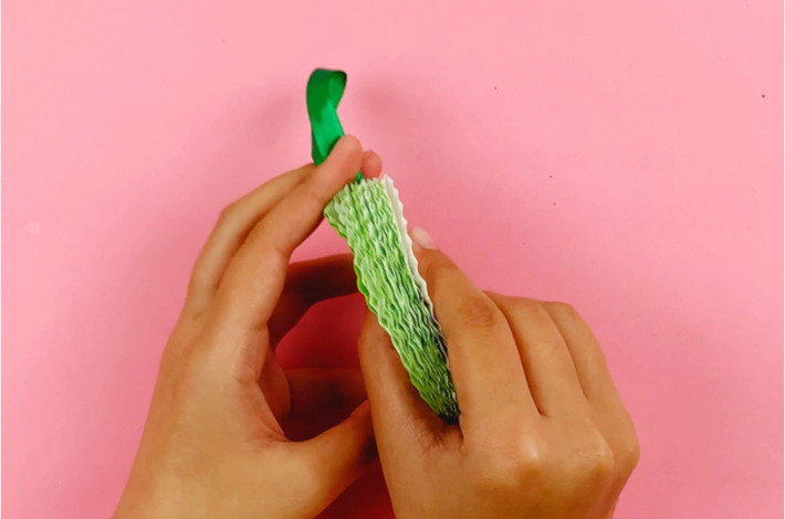 Two hands attaching the green ribbon to the back of the cupcake liners.