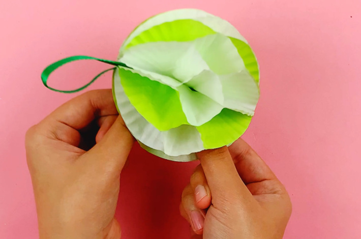 Two hands holding a completed paper ornament made from cupcake holders.