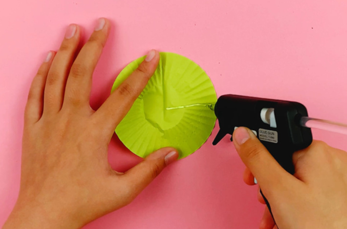 Two hands applying glue from a glue gun to the right hand side in a straight line from the center.