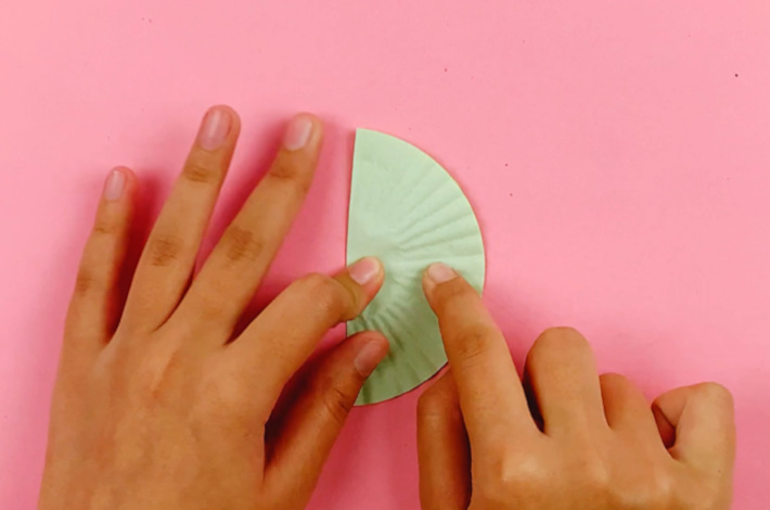 Two hands folding the cup cake liner in half from the left to the right and sticking it down.