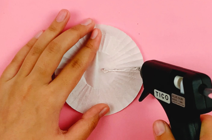 Two hands applying glue from a glue gun to the right hand side in a straight line from the center.