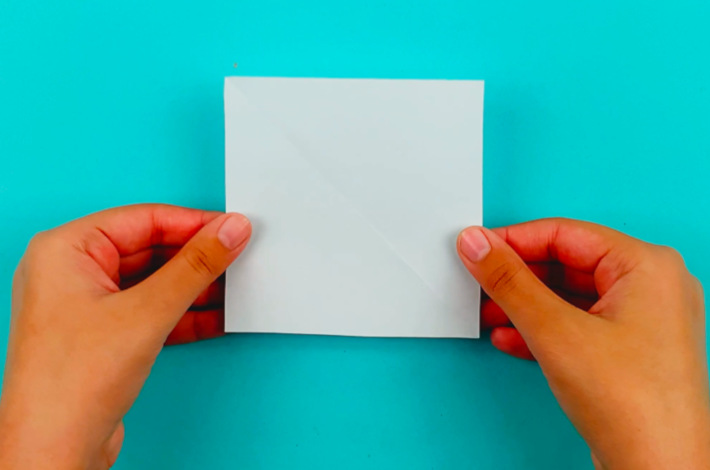Two hands holding a square piece of white paper.