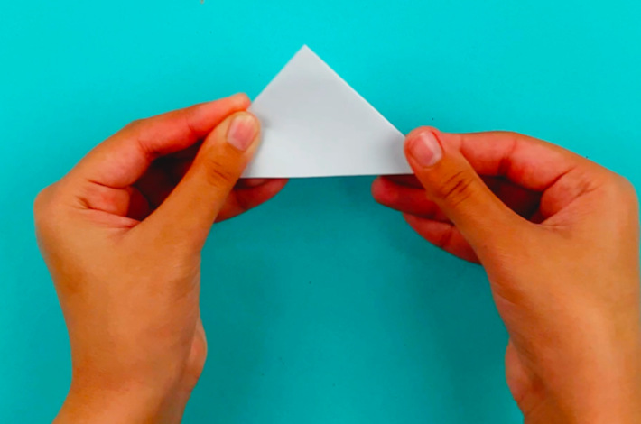 Two hands folding the bigger triangle into a smaller triangle. 