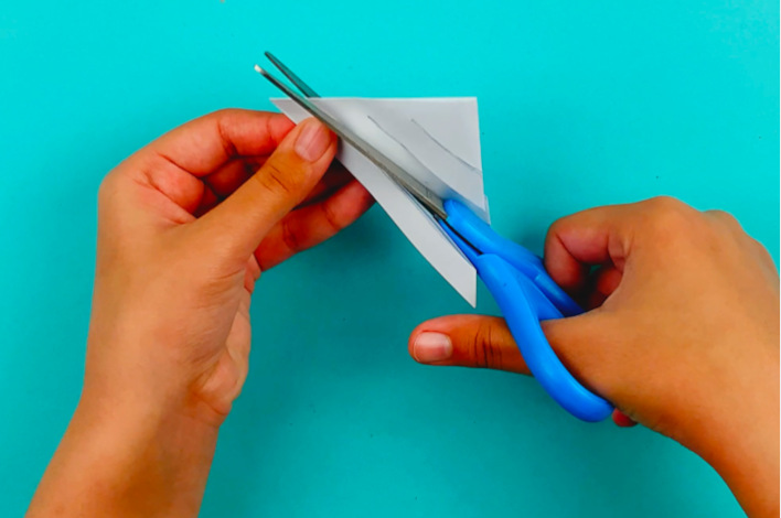 Two hands holding the paper and cutting along the pencil lines with a scissors. 
