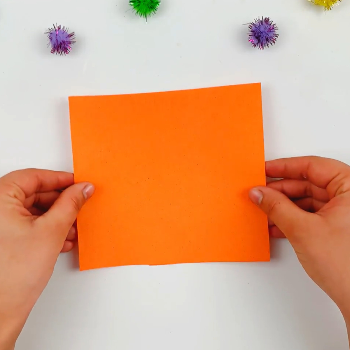 Two hands holding a square piece of orange paper.