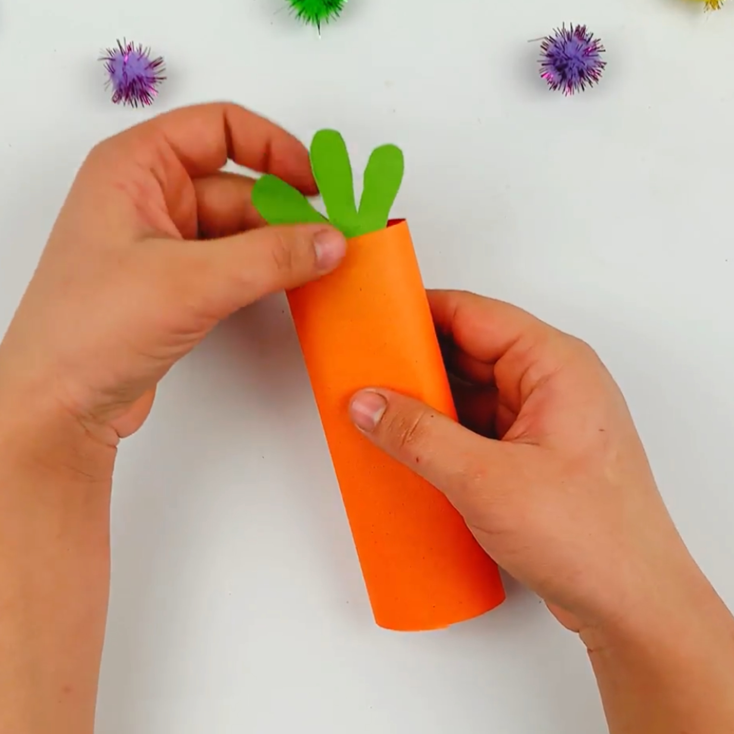 Two hands glueing the top section of the carrot to the orange section.
