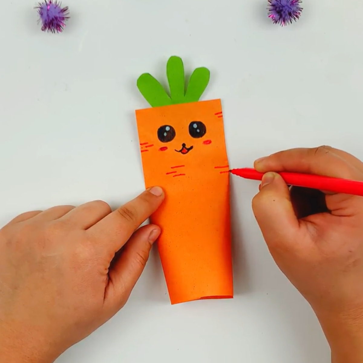 Two hands using colored pens to decorate the carrot. 