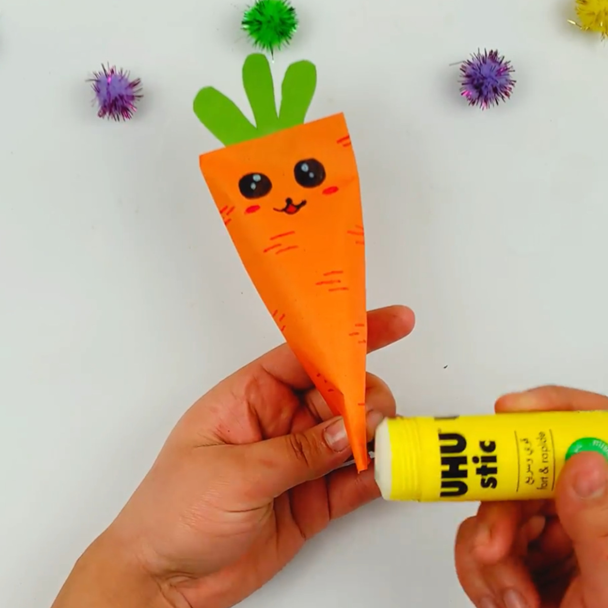 Two hands glueing the bottom of the carrot. 