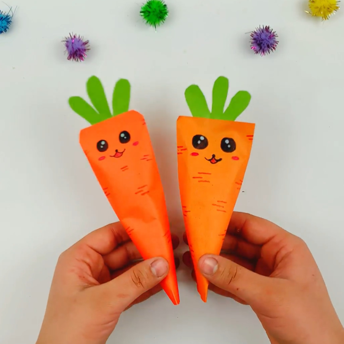 Two hands holding two completed origami carrots.