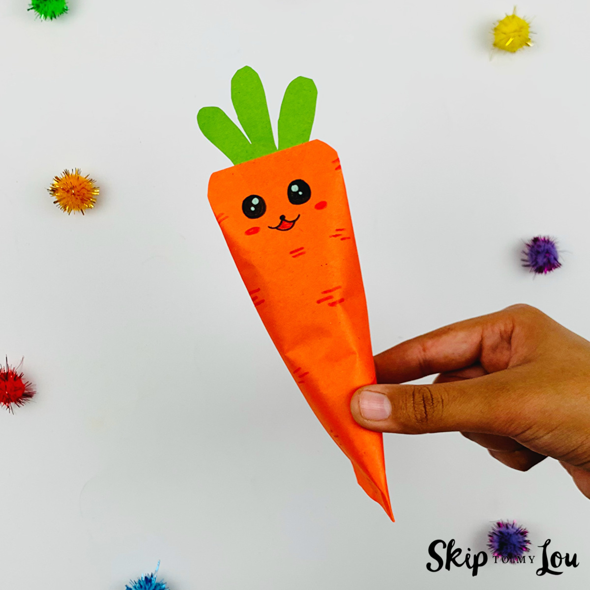 A hand holding an origami carrot made with instructions from Skip to My Lou.