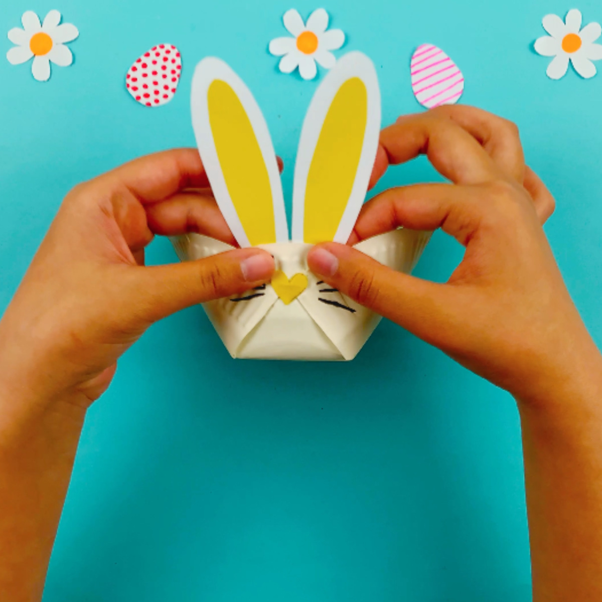Two hands glueing the paper ears onto the paper plate bunny basket.