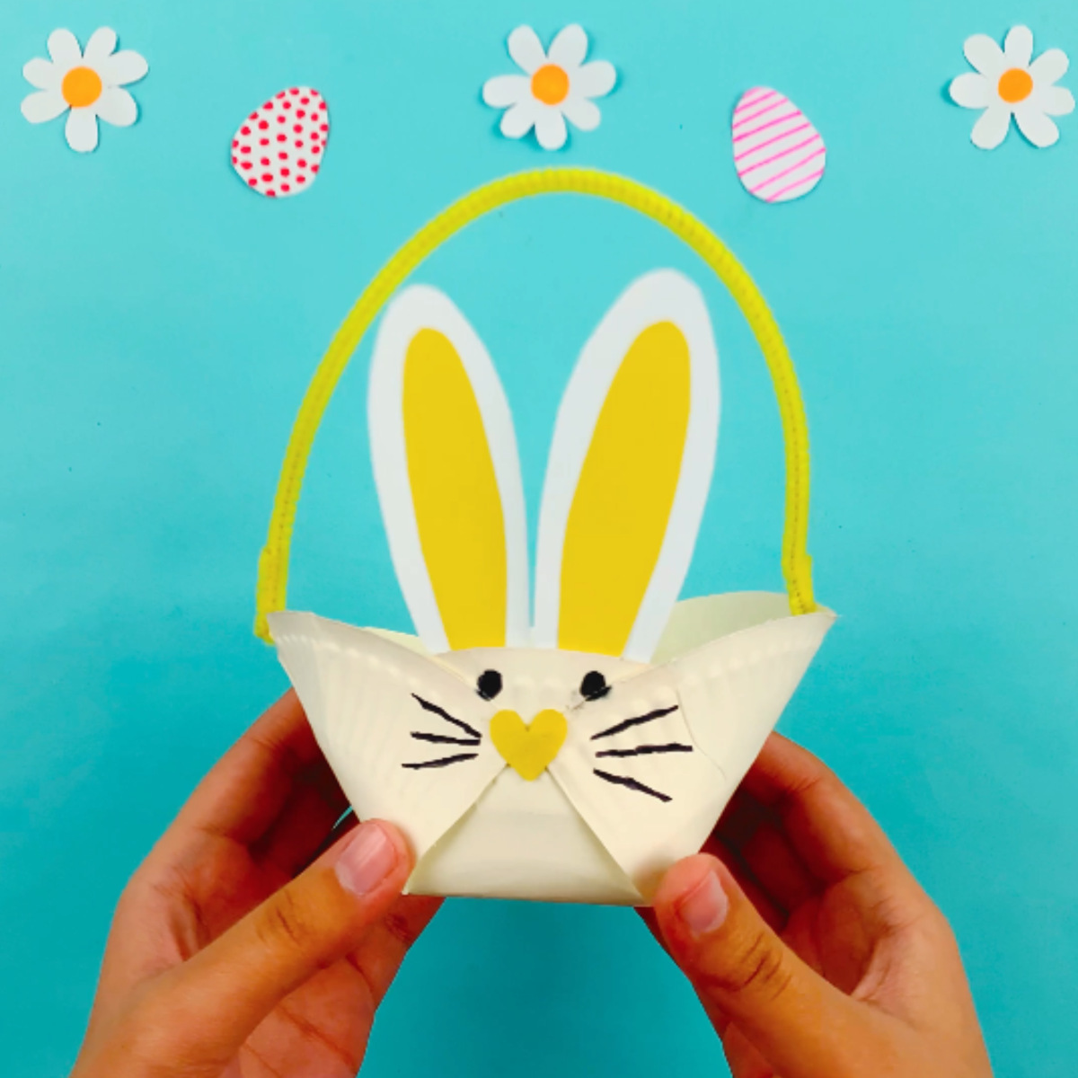 Two hands holding the completed paper plate bunny basket!