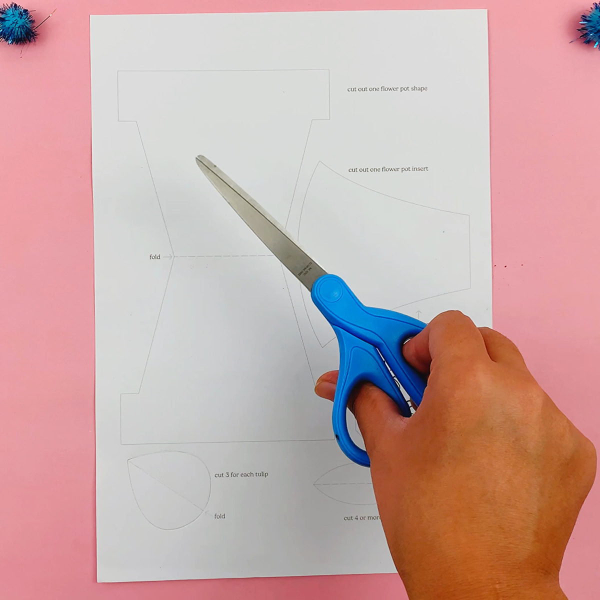 A printed mother's day card template, and a hand holding a pair of scissors ready to cut it out.
