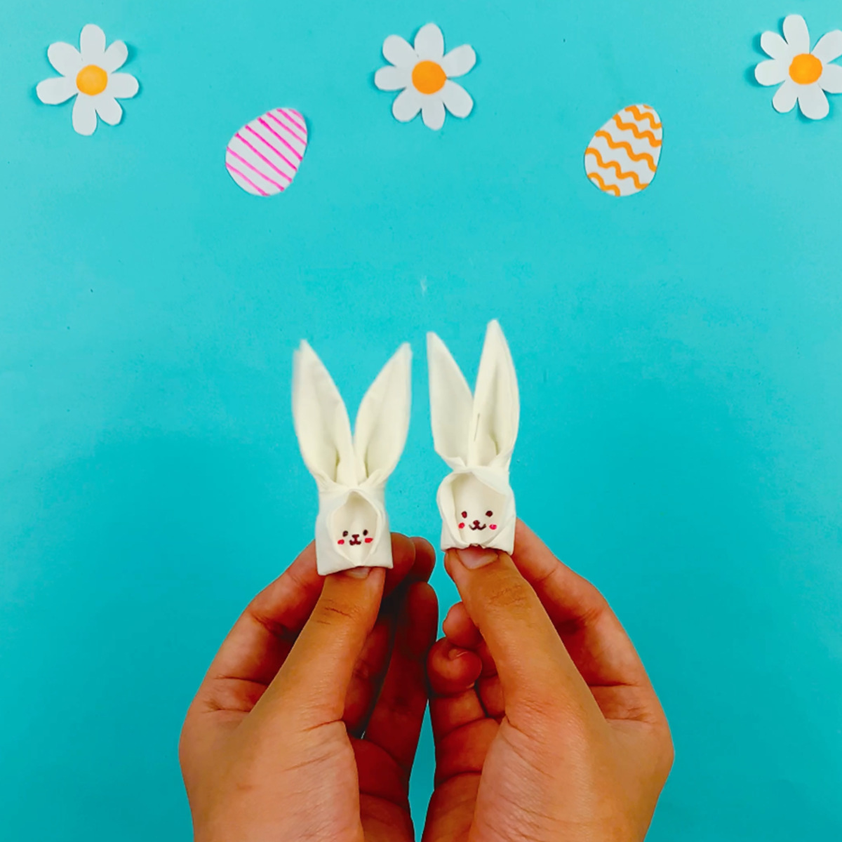 Two hands holding two completed tissue papper bunny finger puppets.
