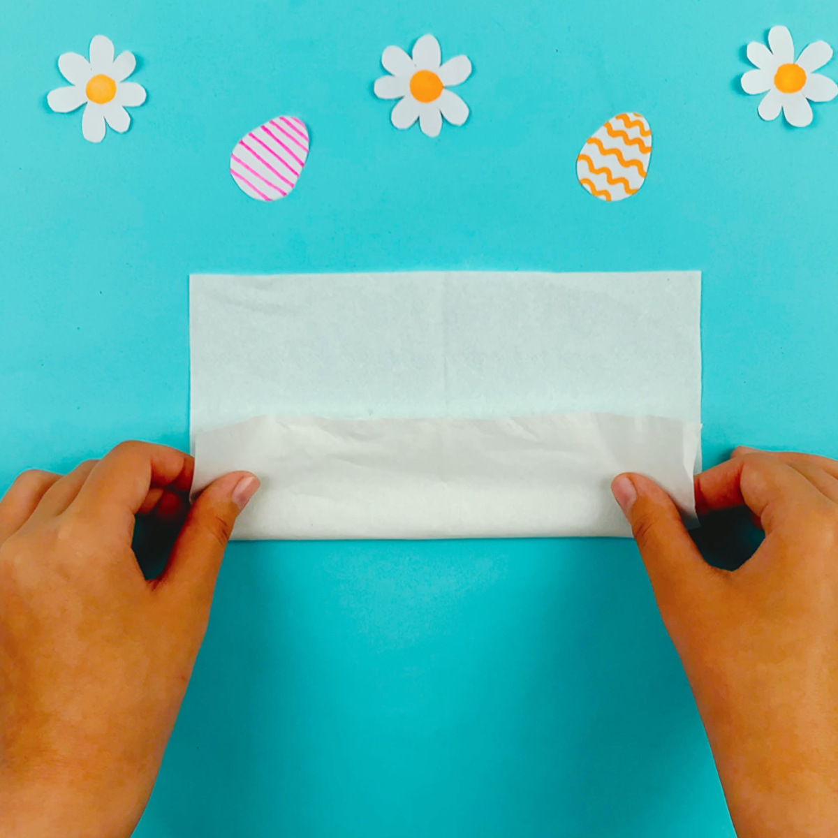 Two hands folding the bottom section of the tissue upwards to just below the halfway point.
