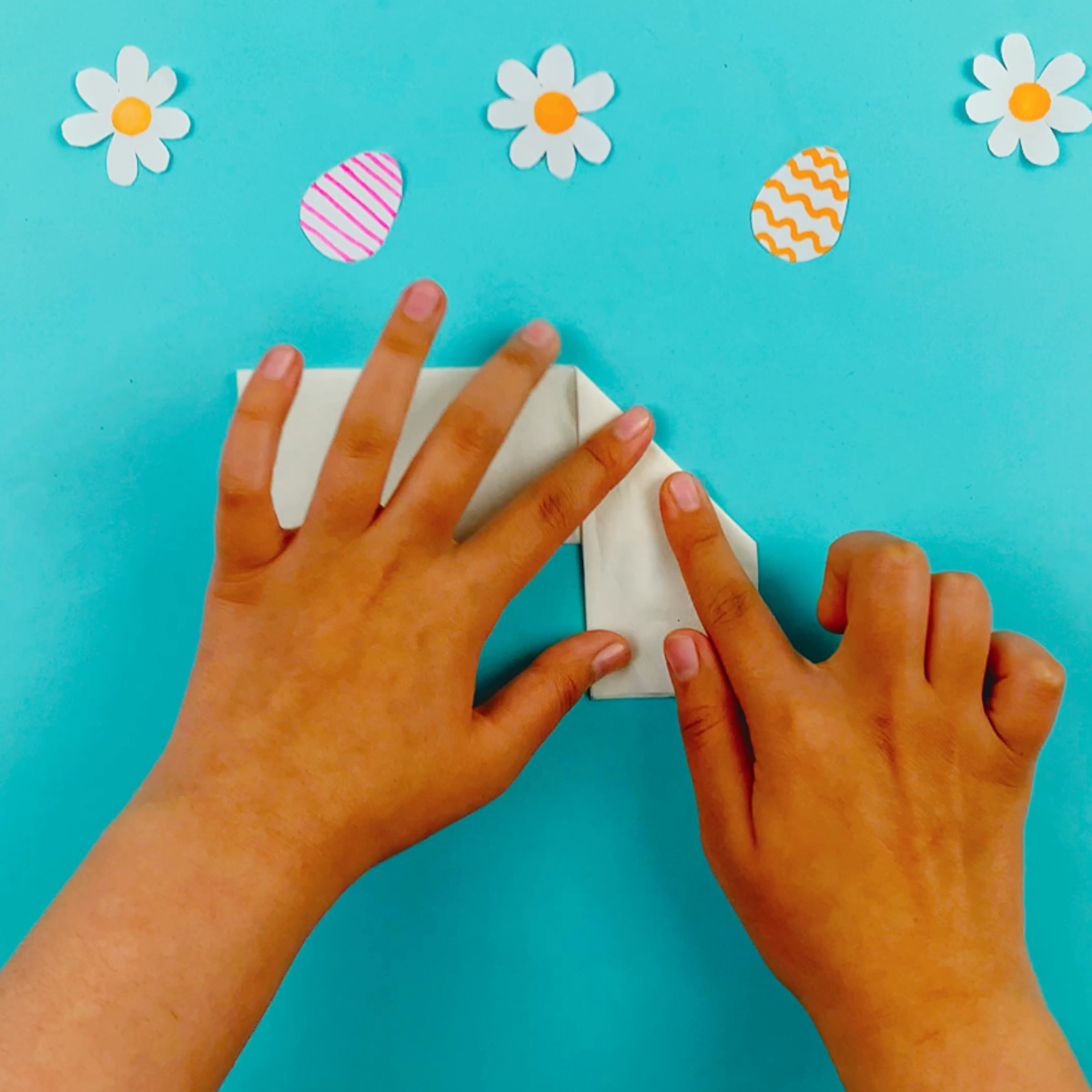 To hands folding the right hand section of the tissue paper down and at a 45-degree angle.