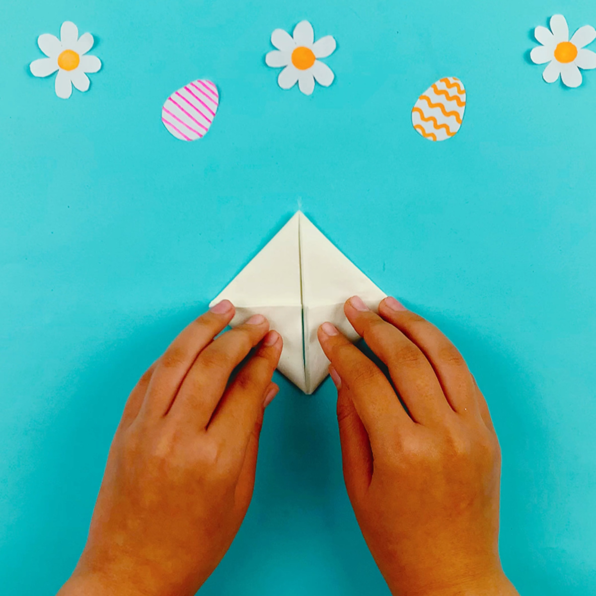 Two hands folding the bottom left-hand and bottom right-hand sections upwards and in to form a kite shape.