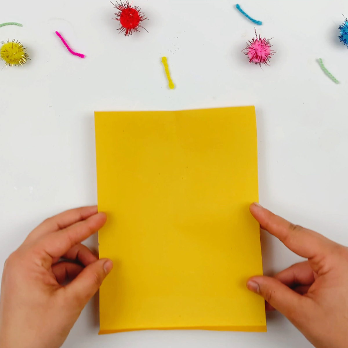 Two hands holding a yellow piece of paper that will form the accordion flower petals.