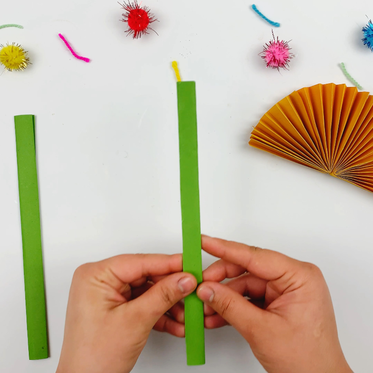 Two hands holding two stems made from folding green paper. 