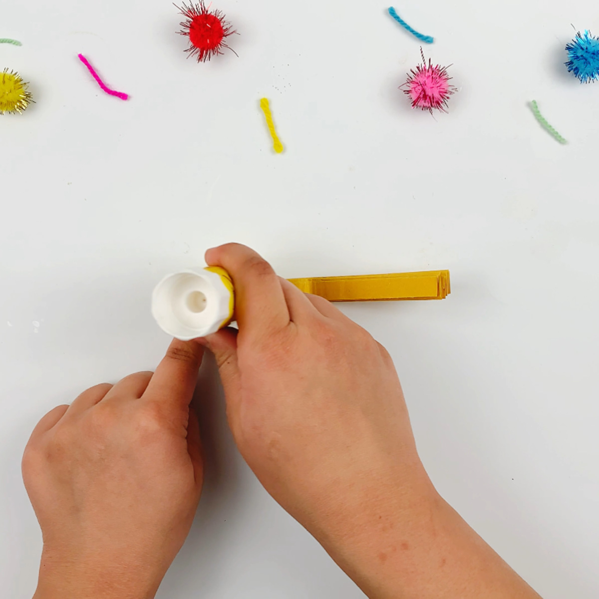 Two hands applying glue to the top of the accordion paper strip.