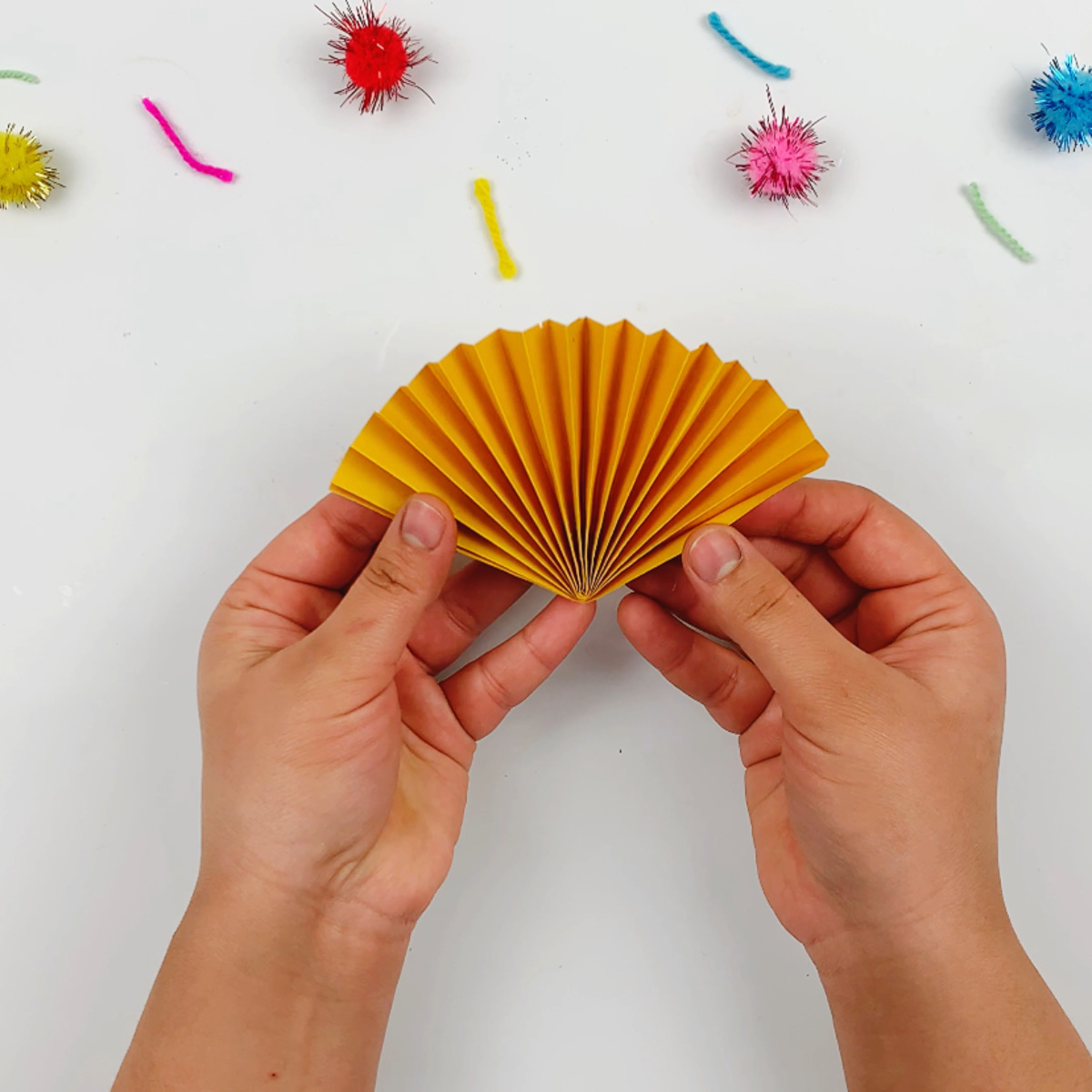 Two hands fanning out the accordion flower petals after sticking the two ends together.