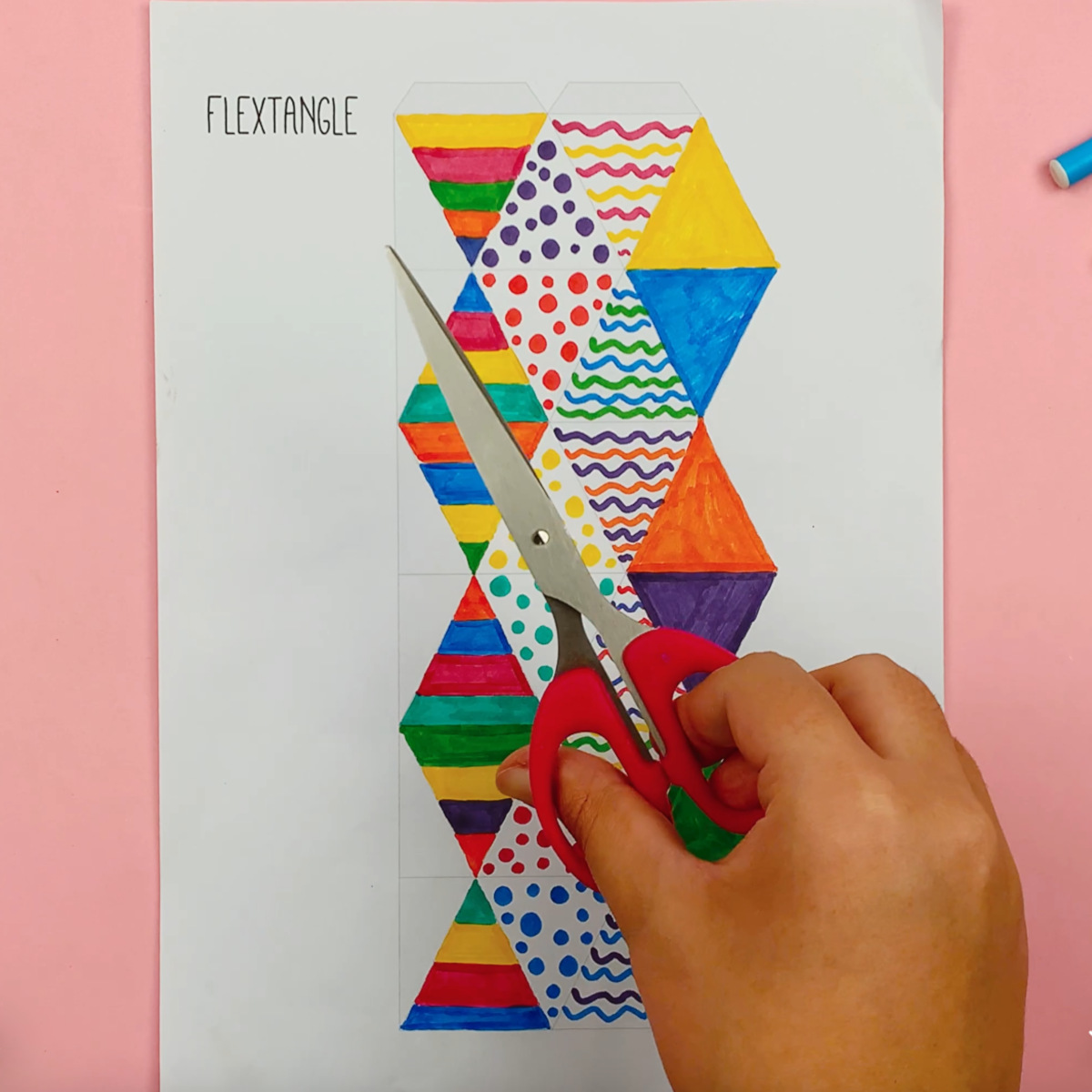 A hand holding a pair of scissors, ready to cut out the flextangle.