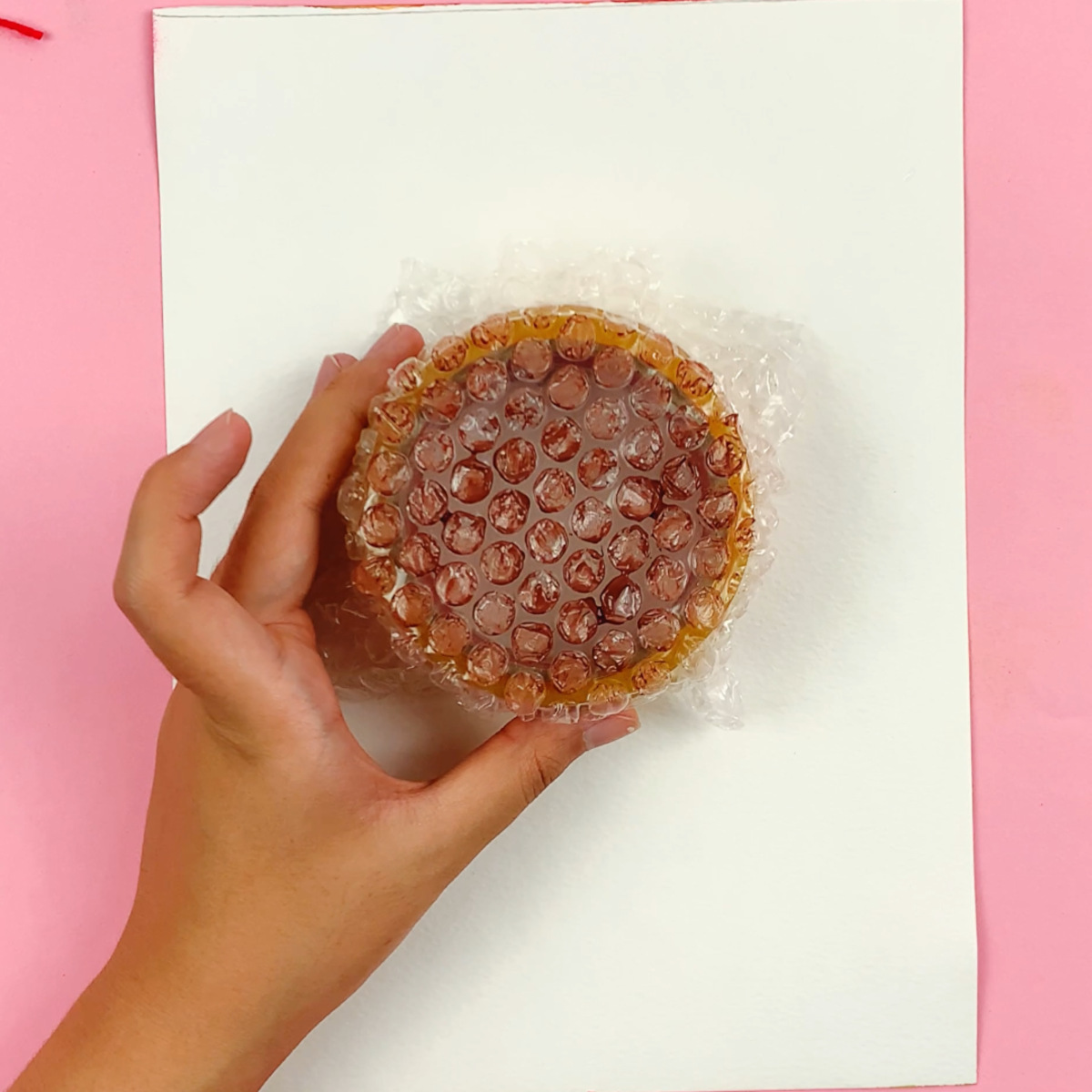 A hand holding the bubble wrap which has been coated in brown paint.