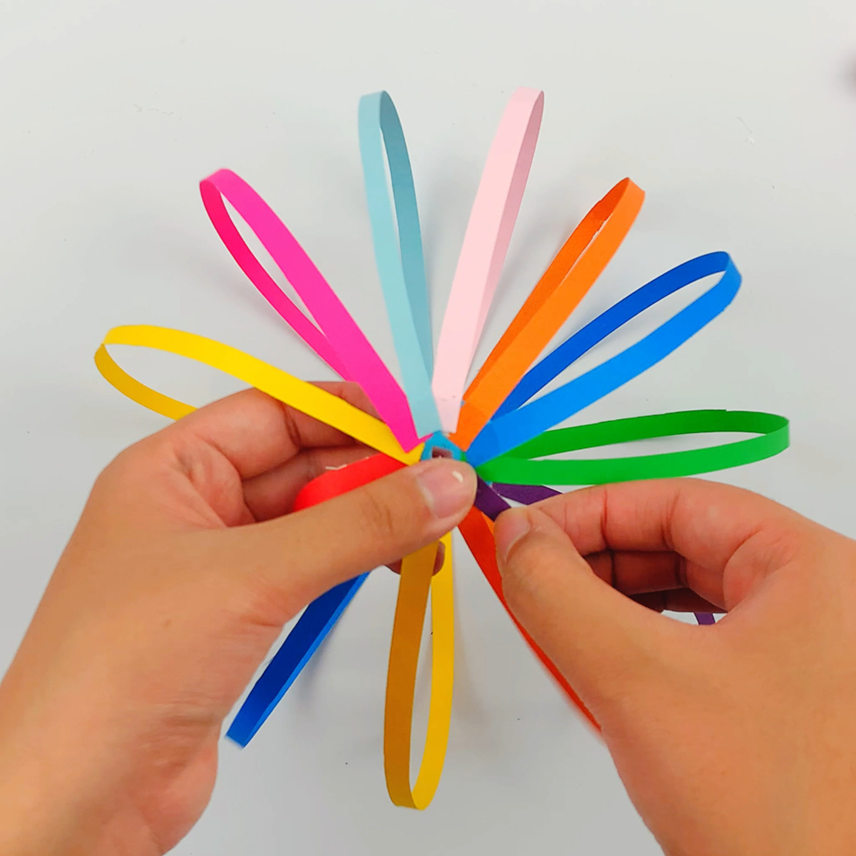 Two hands securing the other ends of the colored paper to the second unpunched circle using some glue.