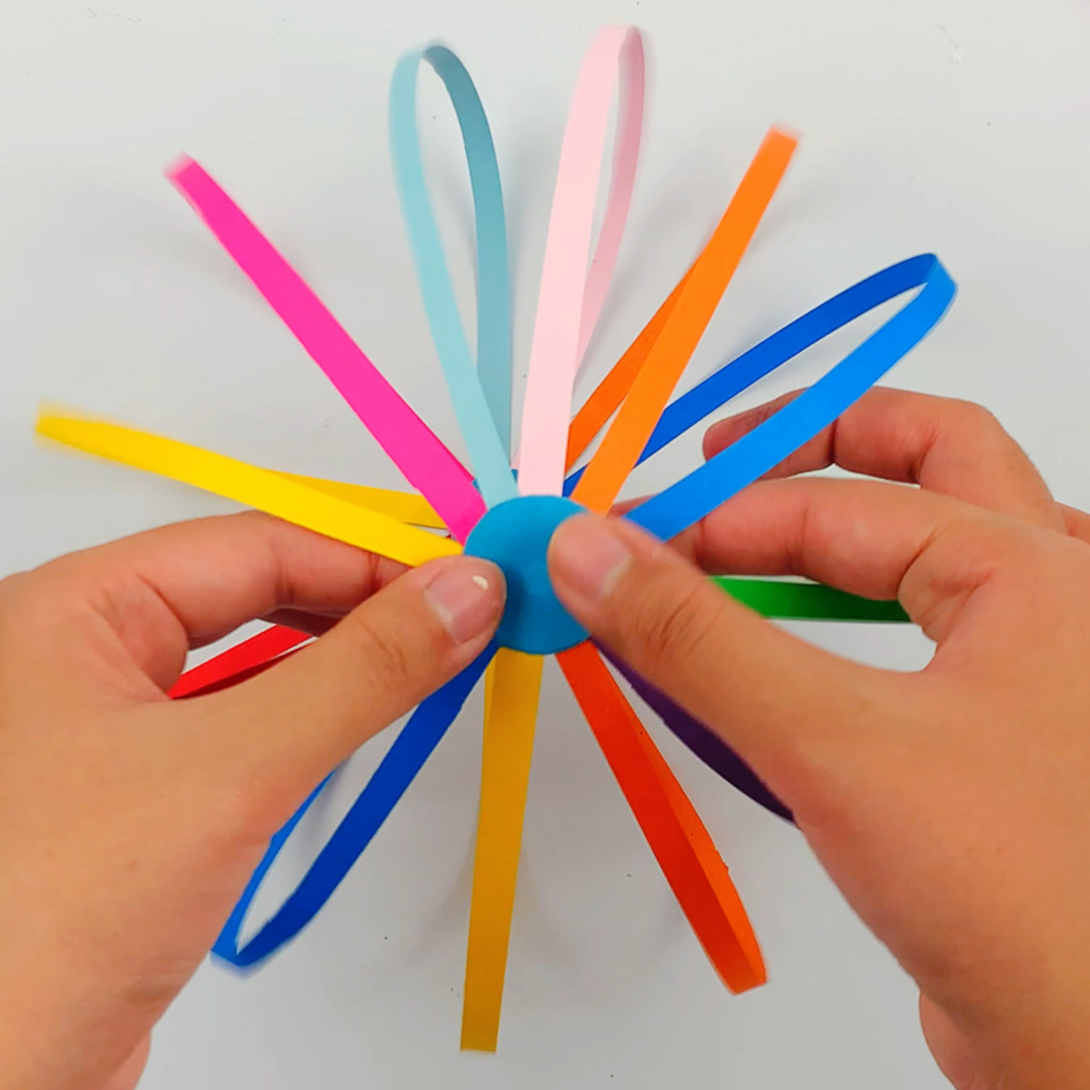 Two hands gluing the other unpunched circle to the top of the rainbow spinner. 