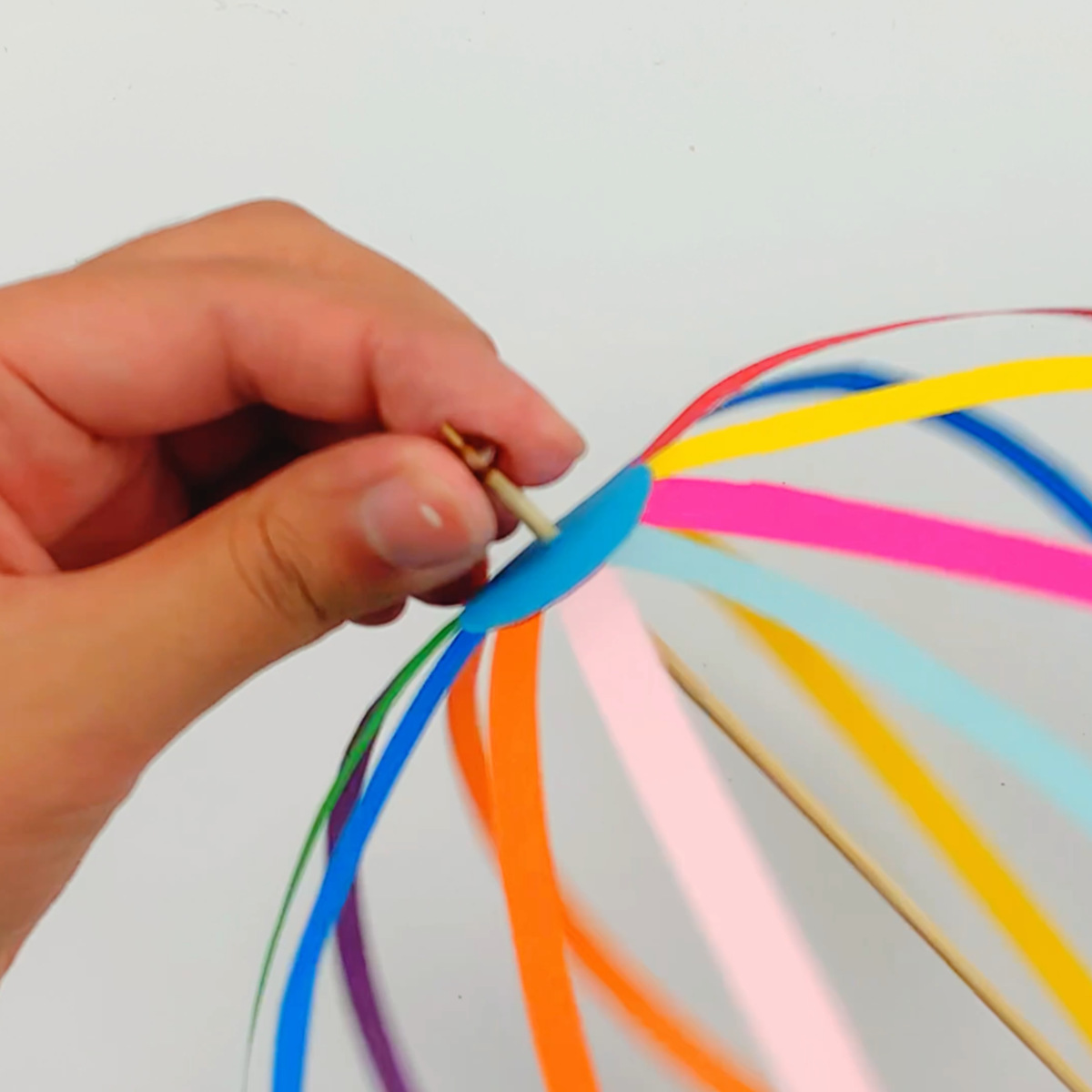 Two hands pushing a skewer stick through the circle at the bottom, all the way to the top, and attaching a bead with a hole in it.