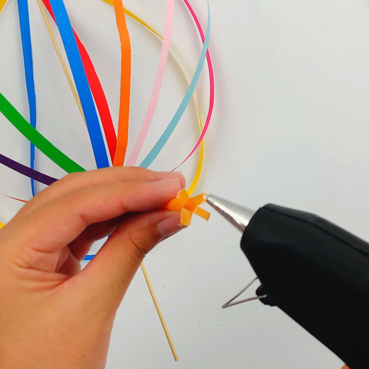 Two hands using a glue gun to place glue on a cut straw.