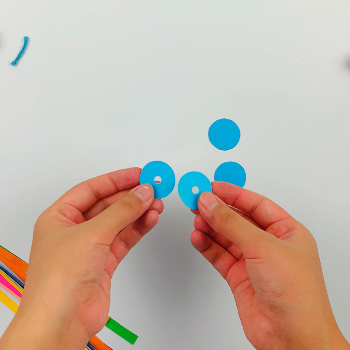 Two hands holding two small circles of blue paper with a hole punched through the middle. 