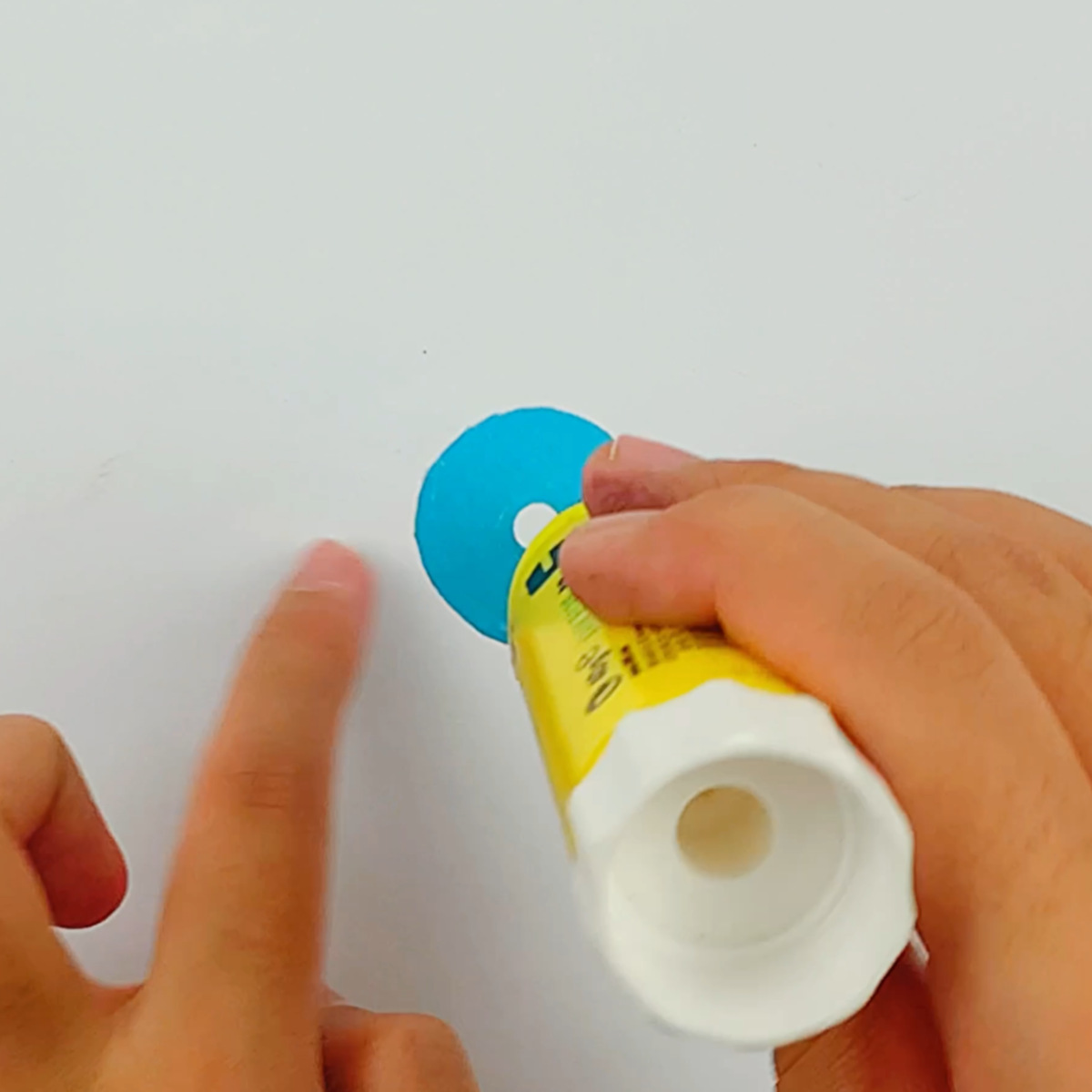 Two hands adding some glue to one of the punched paper circles. 