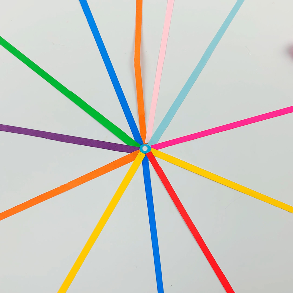 Two hands gluing paper strips all around the circumference of the circle.